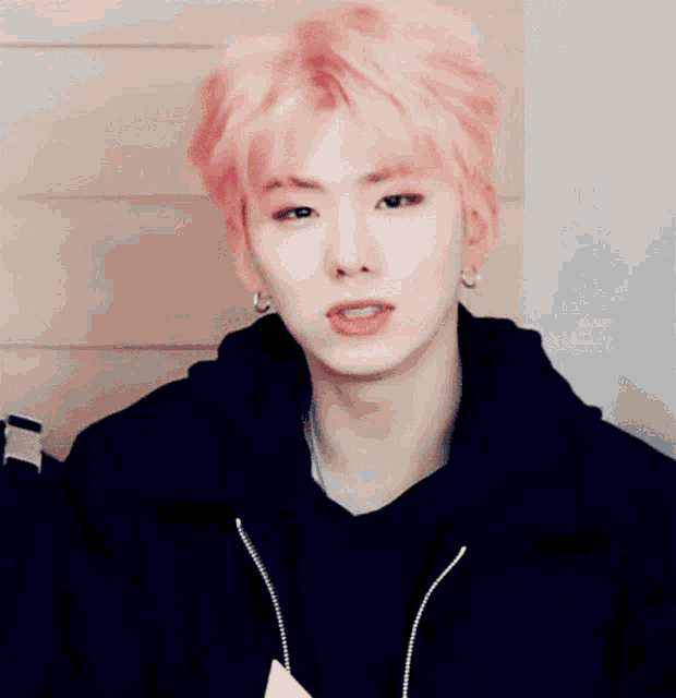 a man with pink hair is wearing a black jacket and earrings