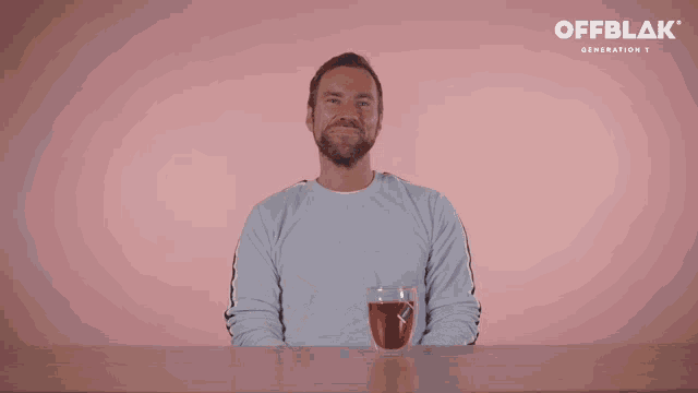 a man sitting at a table with a glass of red liquid in front of a pink wall that says offblak on it