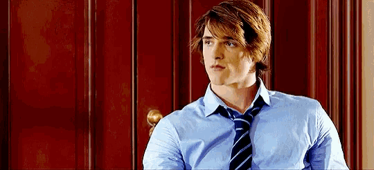 a man in a blue shirt and tie is sitting in front of a wooden wall .