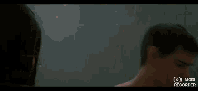 a man without a shirt is standing in a dark room with a mobi recorder on the bottom of the screen .