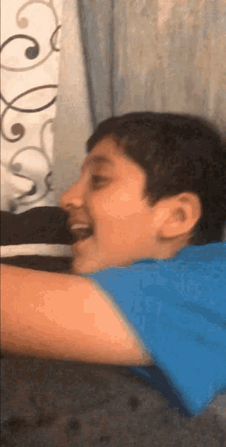 a young boy in a blue shirt is laying on a couch