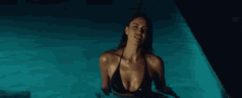 a woman in a bikini is swimming in a pool at night .