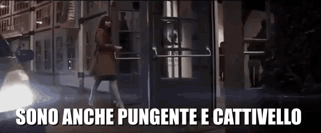 a woman is walking in front of a building with the words sono anche pungent e cattivello written on the bottom
