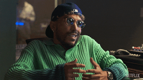 a man wearing sunglasses and a green sweater is sitting in front of a netflix monitor