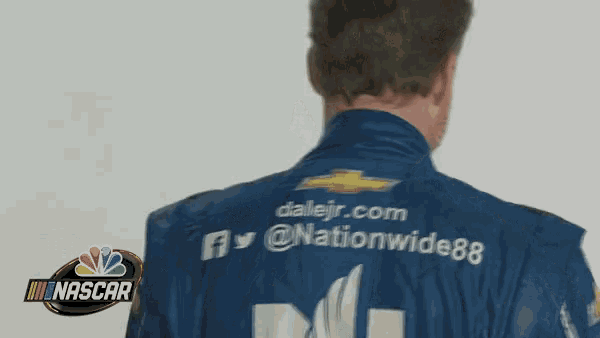 a man wearing a nascar jacket is talking on a phone
