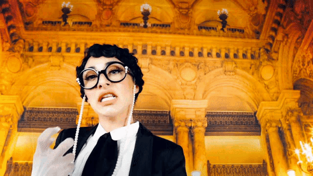 a woman wearing glasses and a pearl necklace is standing in front of a building