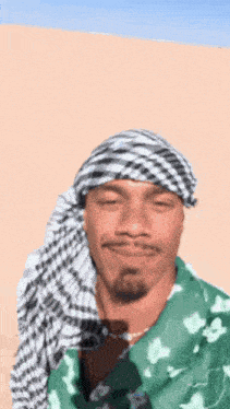a man wearing a head scarf and a green shirt is standing in the desert
