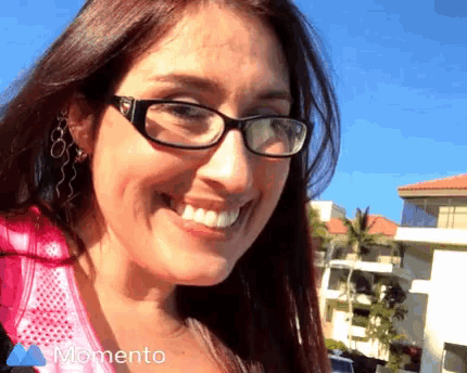 a woman wearing glasses and earrings smiles in front of a blue sky