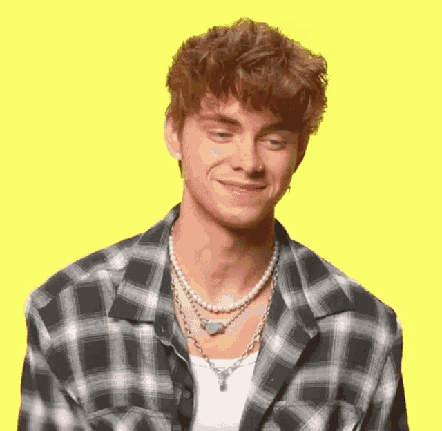 a young man is wearing a plaid shirt and a pearl necklace .