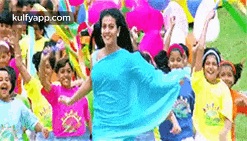 a woman in a blue saree is dancing in front of a group of children .
