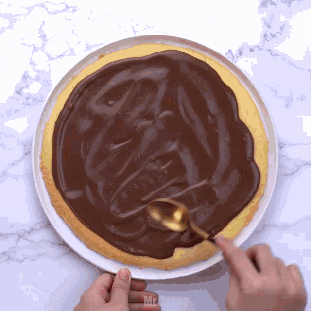 a person spreading chocolate sauce on a pizza with a spoon