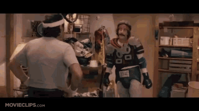 two men are standing next to each other in a room . one of the men is wearing a superhero costume .