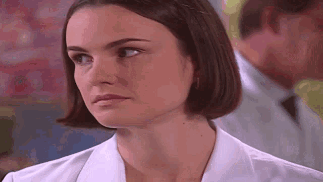 a woman in a white lab coat is looking at the camera with a serious look on her face .