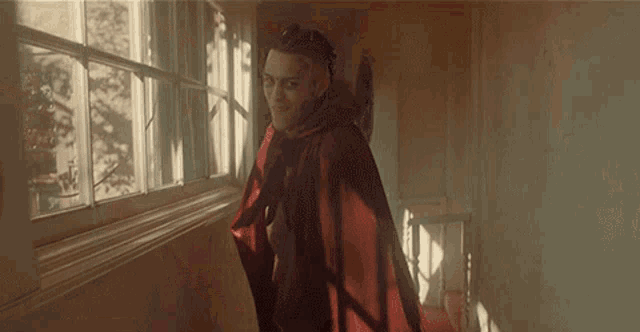 a man in a red cape is standing in front of a window