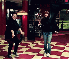 two women are dancing on a checkered floor in front of a sign that says exit