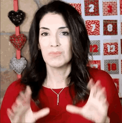a woman in a red dress is making a face with her hands in front of a calendar with hearts on it .