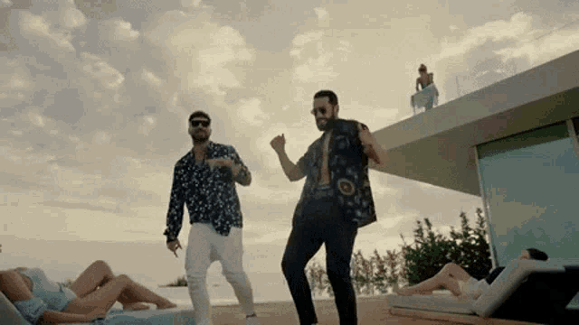 two men are dancing in front of a woman laying on a lawn chair