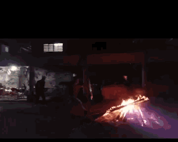 a group of people are standing around a fire in a dark room