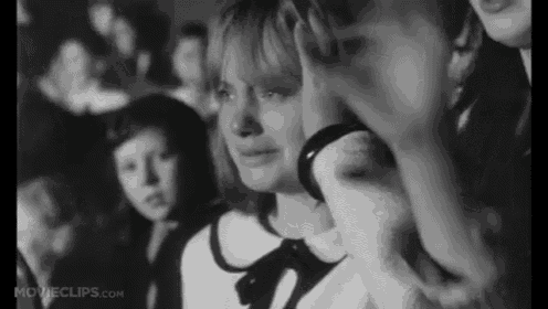 a woman is crying in a black and white photo while sitting in a crowd of people .