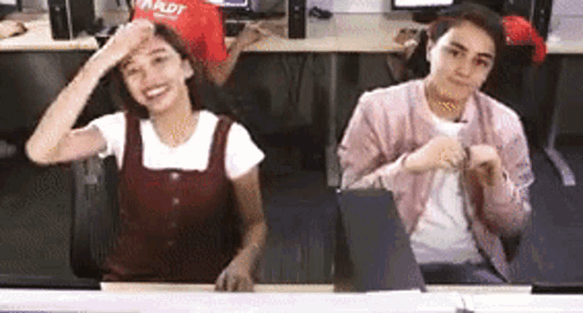 two women are sitting at a desk with their hands on their heads .