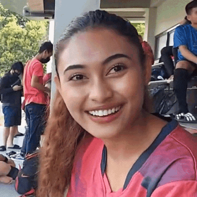 a woman in a red shirt is smiling at the camera while sitting on a porch .