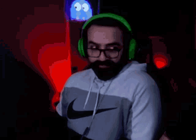 a man with a beard and glasses is wearing green headphones and a nike shirt .