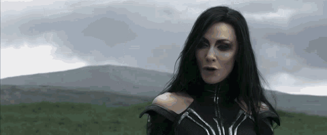 a woman with long black hair is standing in a field with a mountain in the background .