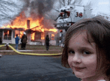 a little girl is standing in front of a burning house with a fire truck in the background .