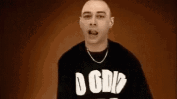 a bald man wearing a black shirt with the word gdp on it is standing in front of a brown background .