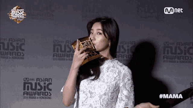 a woman is holding a trophy in front of a wall that says music awards
