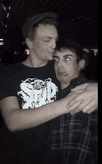 a man wearing a shirt that says ' scum ' on it is hugging another man in a plaid shirt