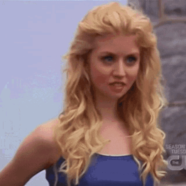 a woman with blonde hair is wearing a blue tank top and earrings .