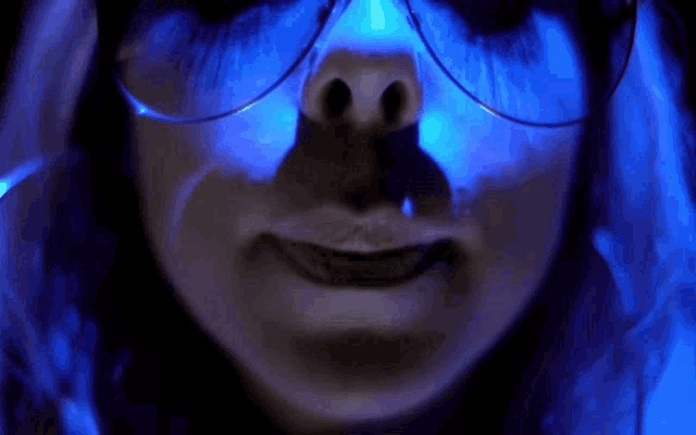 a close up of a woman 's face with glasses and blue light behind her