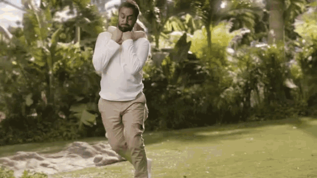 a man in a white shirt and khaki pants is jumping in the air .
