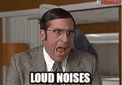 a man in a suit and tie is screaming with his mouth open and the words `` loud noises '' written next to him .