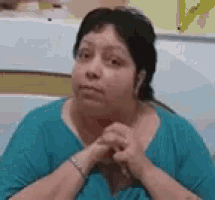 a woman in a blue shirt is sitting down with her hands folded .