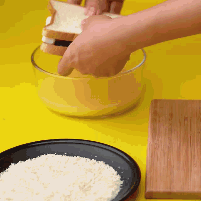 a person is dipping a slice of bread in a bowl of bread crumbs