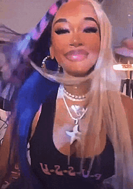 a woman with long blonde hair is wearing a black tank top and a necklace .