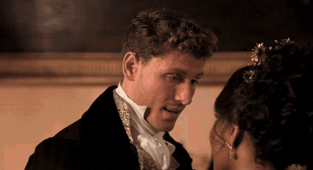 a man in a suit and tie looks at a woman in a tiara