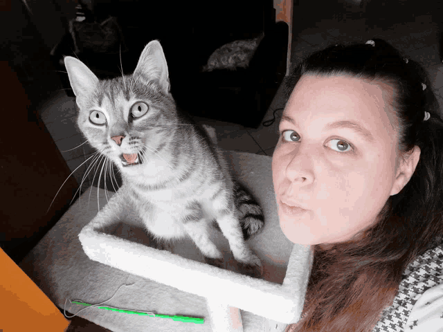 a woman is standing next to a cat that is looking at the camera
