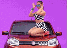 a woman kneeling on the hood of an orange car