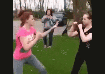 two women are fighting in the grass with a woman standing behind them