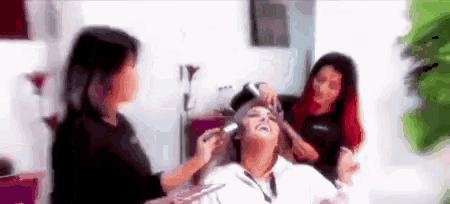 a woman is getting her hair done in a salon while another woman applies makeup to her face .