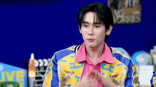 a young man wearing a colorful jacket and a pink shirt is sitting in front of a blue wall .