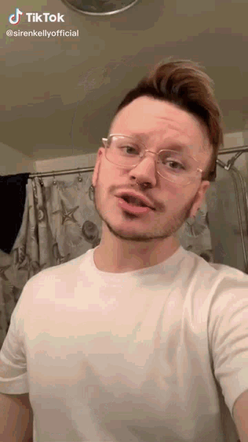 a man wearing glasses and a white shirt is taking a selfie in front of a shower curtain