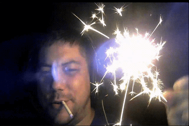 a man smoking a cigarette and holding a sparkler in his hand