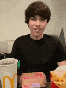 a young man is sitting at a table with a mcdonald 's box and a cup of soda