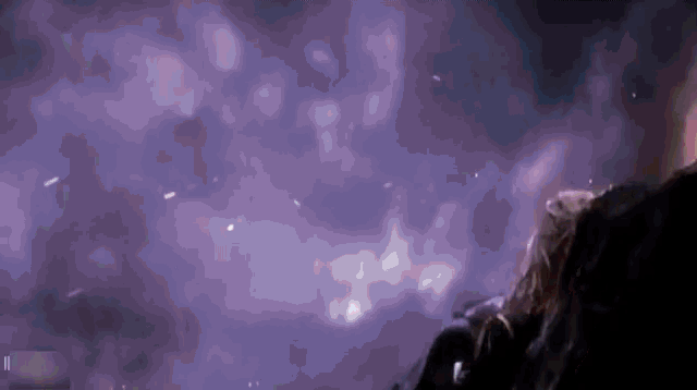 a person is standing in a dark room with a purple background and smoke coming out of it .