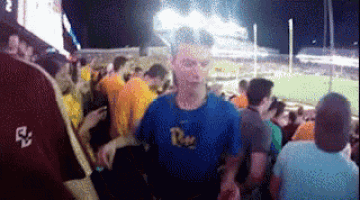 a man in a blue shirt with the letter r on it stands in a crowd