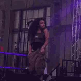 a woman is jumping in the air on a stage with her hands in the air .